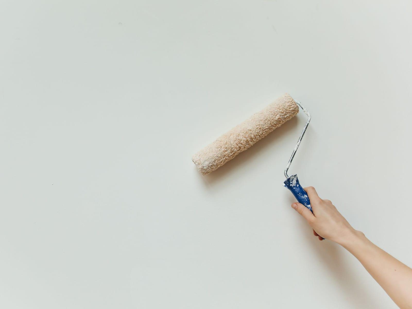 Farbrolle trägt weiße Wandfarbe auf eine Innenwand auf